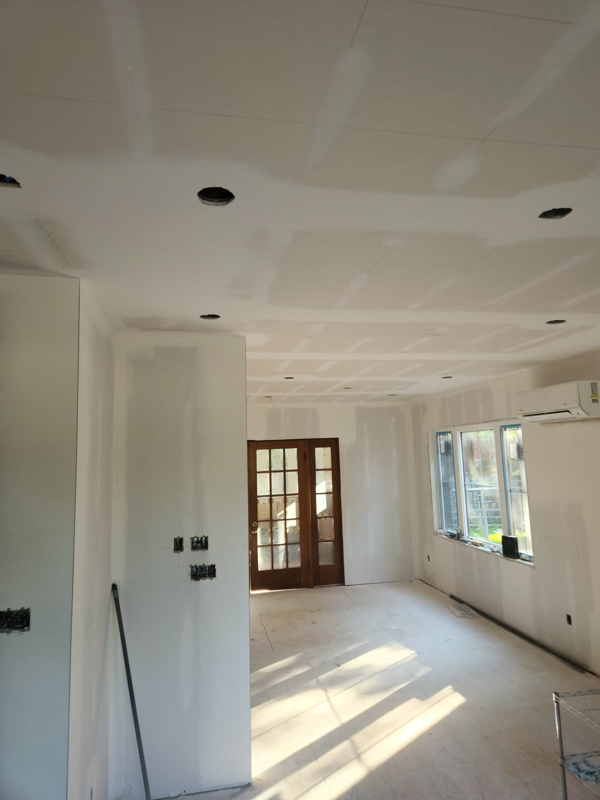 Open main-floor room with taped and mudded ceiling and wall joints, French doors and windows at the far end